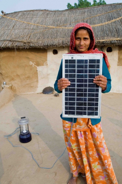 An Indian girl in a headscarf stands facing the camera, holding a solar panel. 