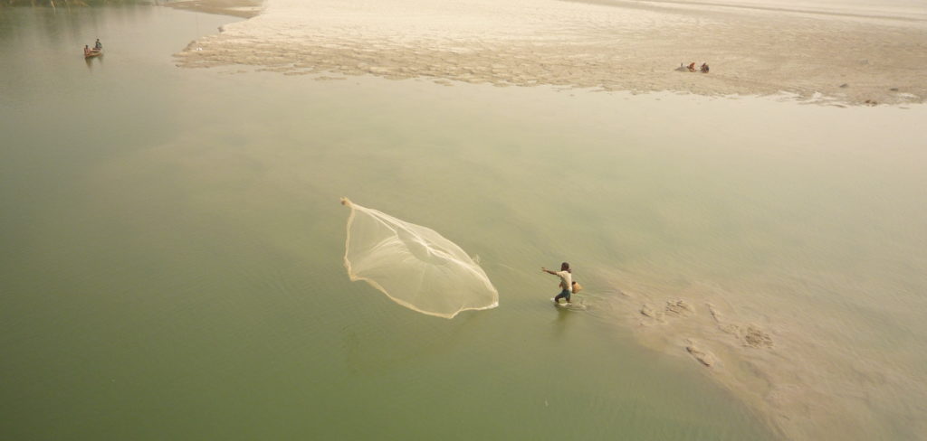 A man casts a large fishing net out into Teesta river.