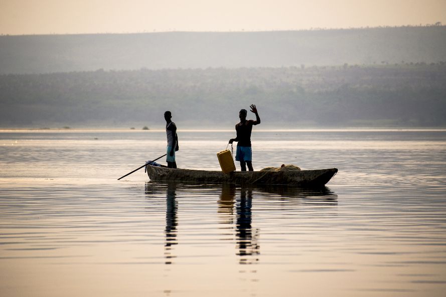 Two fisherman in a small boat on the Congo River. One is waving to the camera.