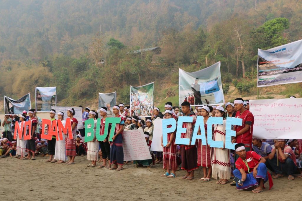 A group of people protesting, hold up signs spelling out the words no dam but peace.