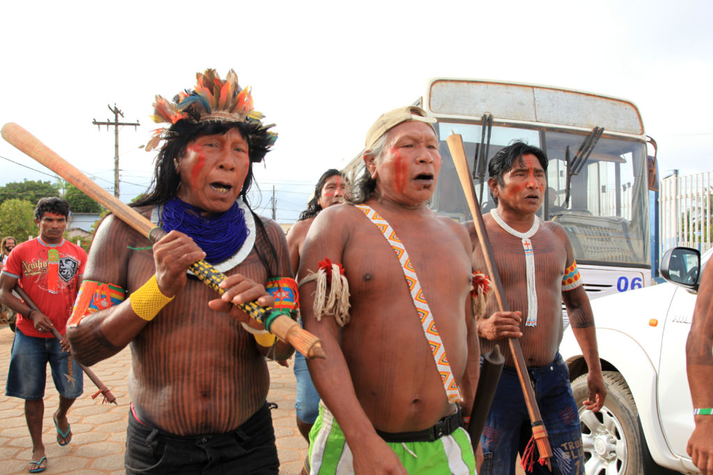 Three male Xikrin Kayapo leaders, walking off camera, holding sticks. 