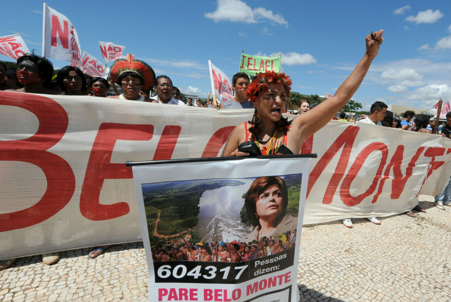 A woman with her fist raised is in the foreground, behind her are people protesting. 